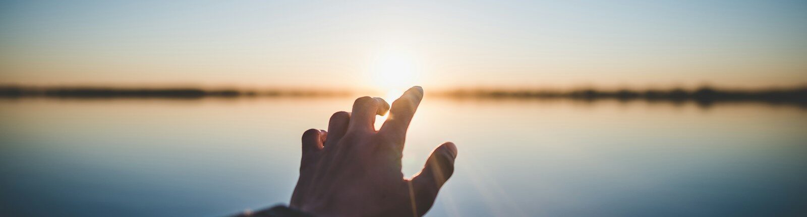 landscape photography of person's hand in front of sun
